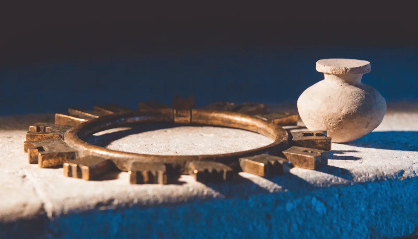 A ring of bronze keys on a stone ledge beside a small sealed clay vessel.